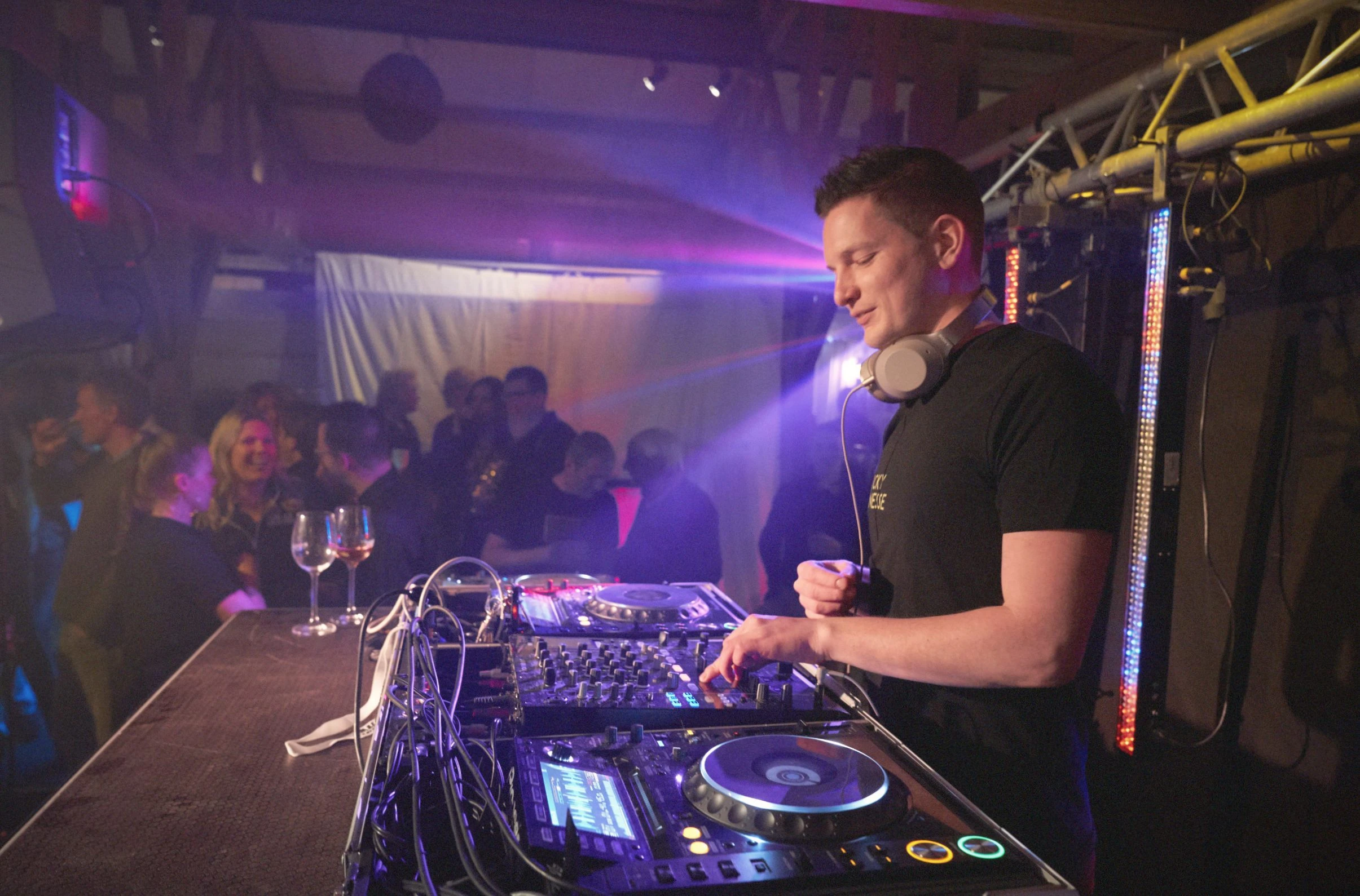 DJ draait achter mengpaneel op Afstudeerfeest met koptelefoon onder paarse lichteffecten