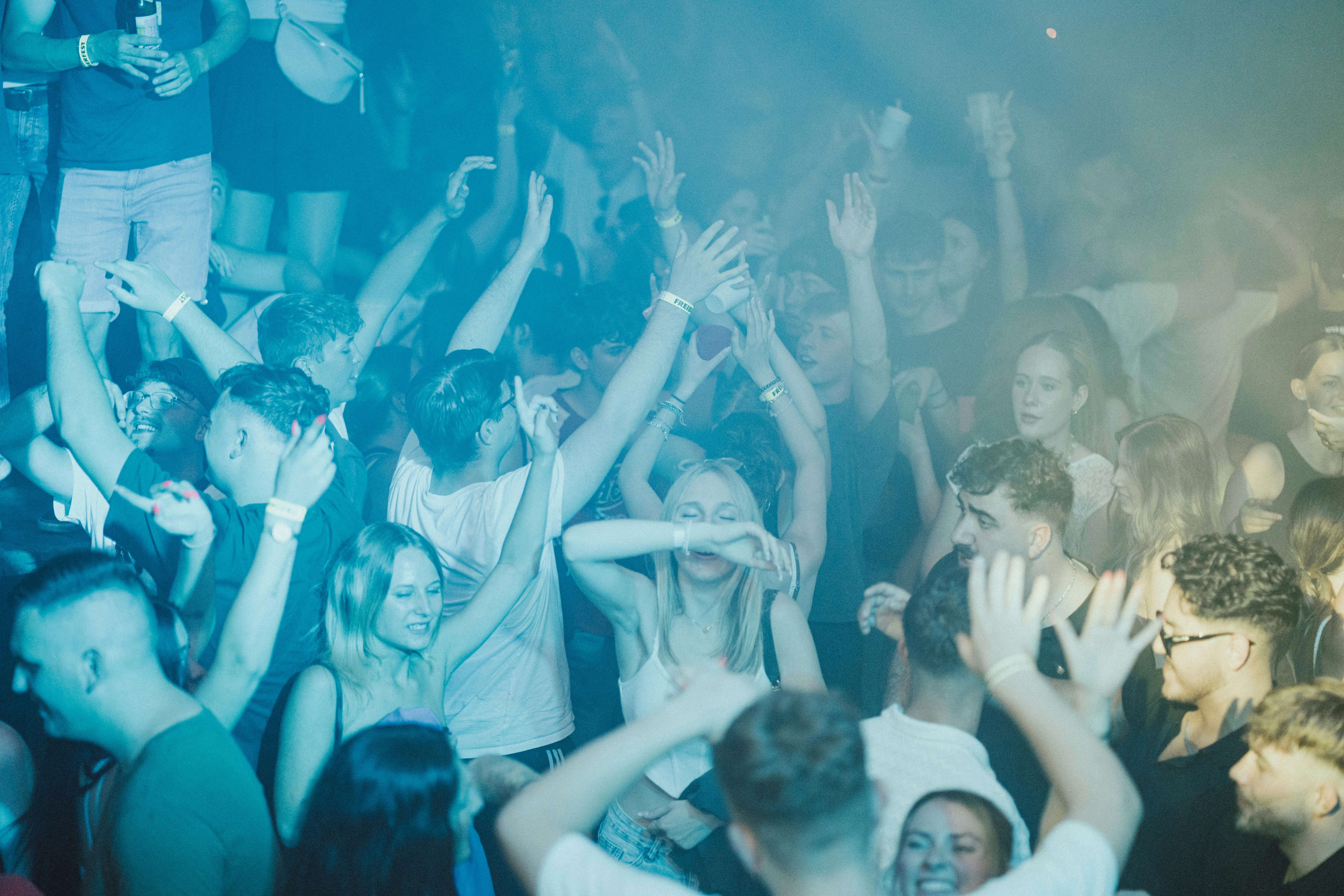 Menigte danst op Afstudeerfeest onder blauwe verlichting met handen omhoog
