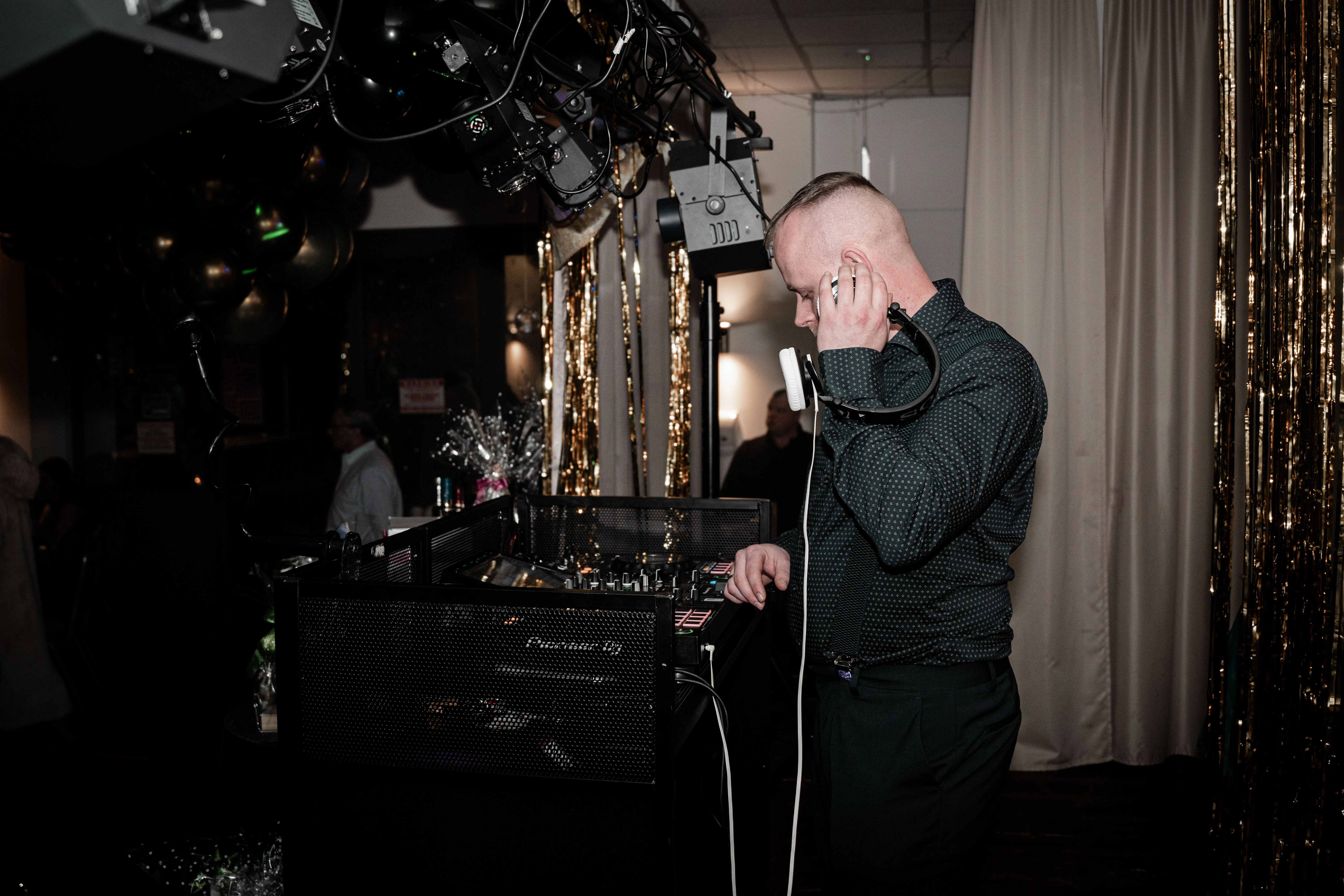 DJ draait achter decks op Afstudeerfeest met koptelefoon en gouden decoratie op achtergrond