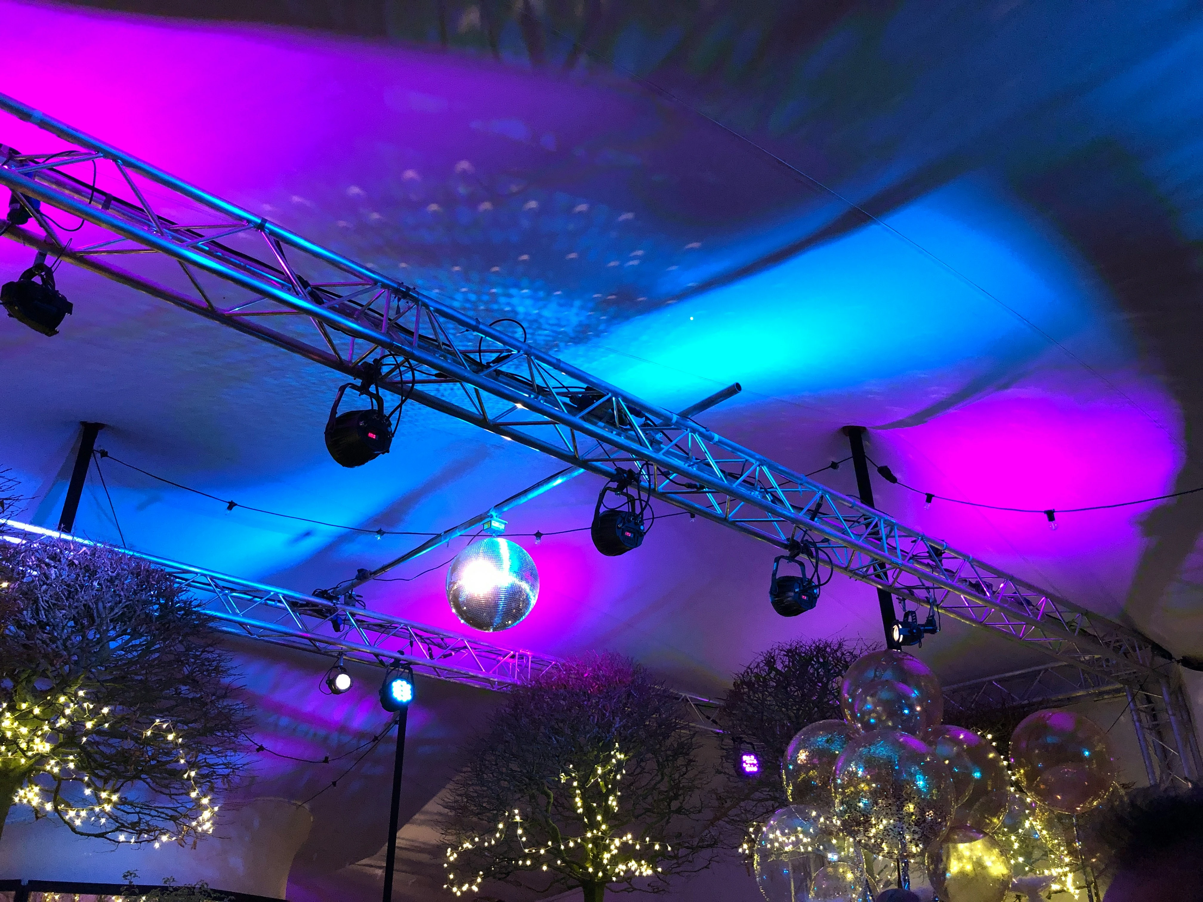 Feesttent aangekleed voor gala met trussconstructie, gekleurde verlichting, discobal en verlichte ballonnen