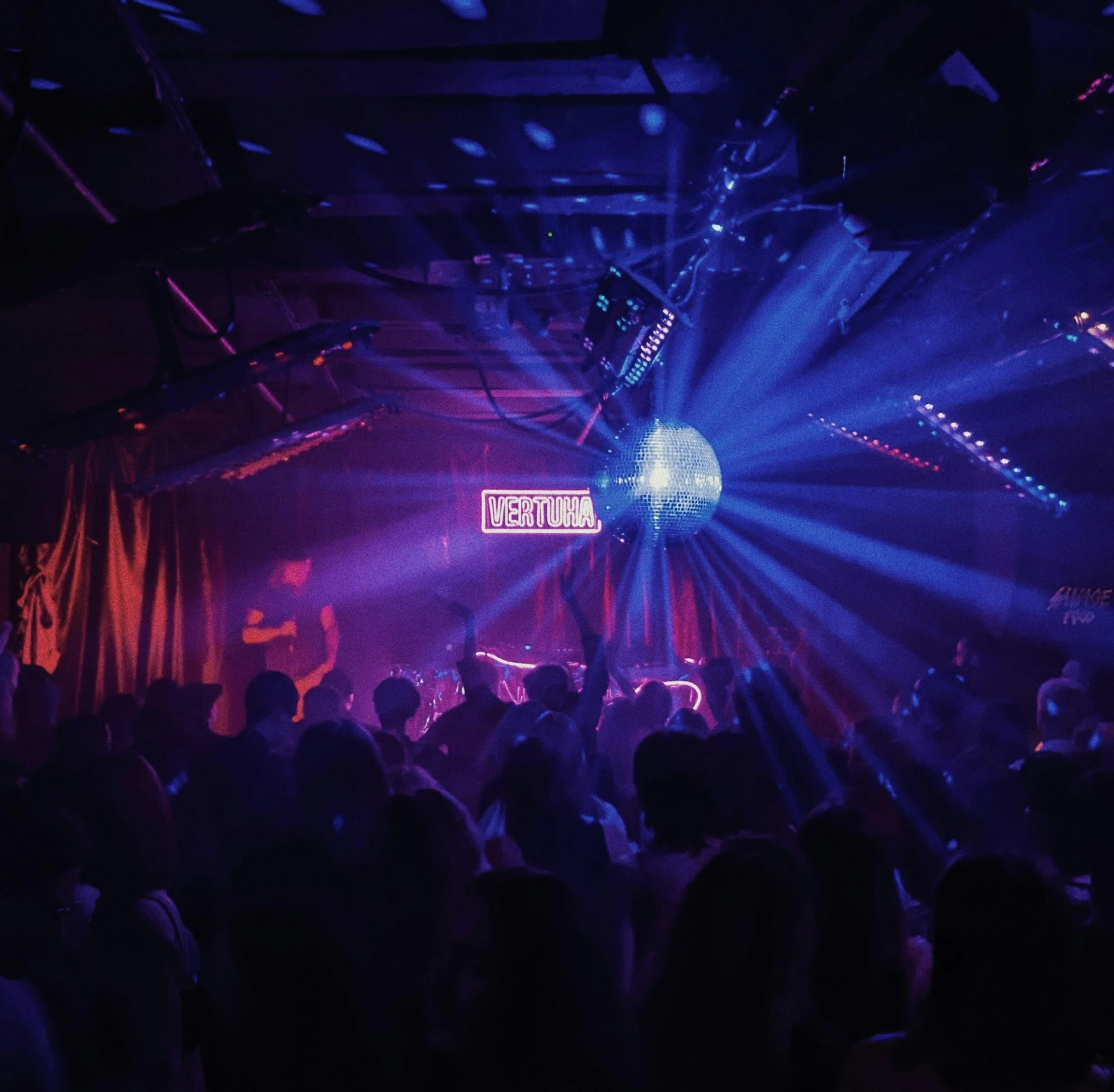 Menigte danst op dansvloer onder blauw en rood licht met discobol in clubsetting