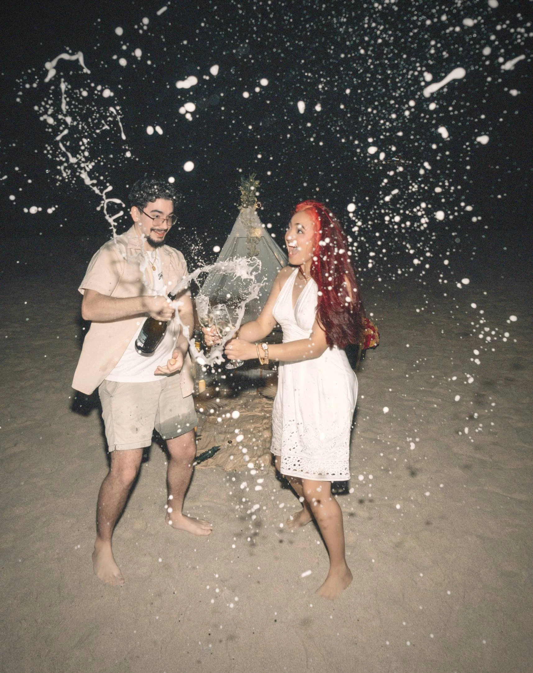 Man en vrouw strooien champagne op strand in het donker