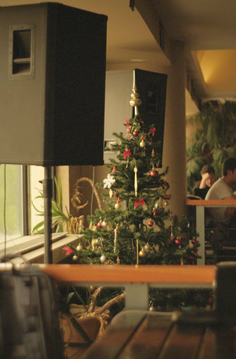 Kerstboom versierd met rode en gouden ballen in ruimte met professionele luidsprekers op statieven