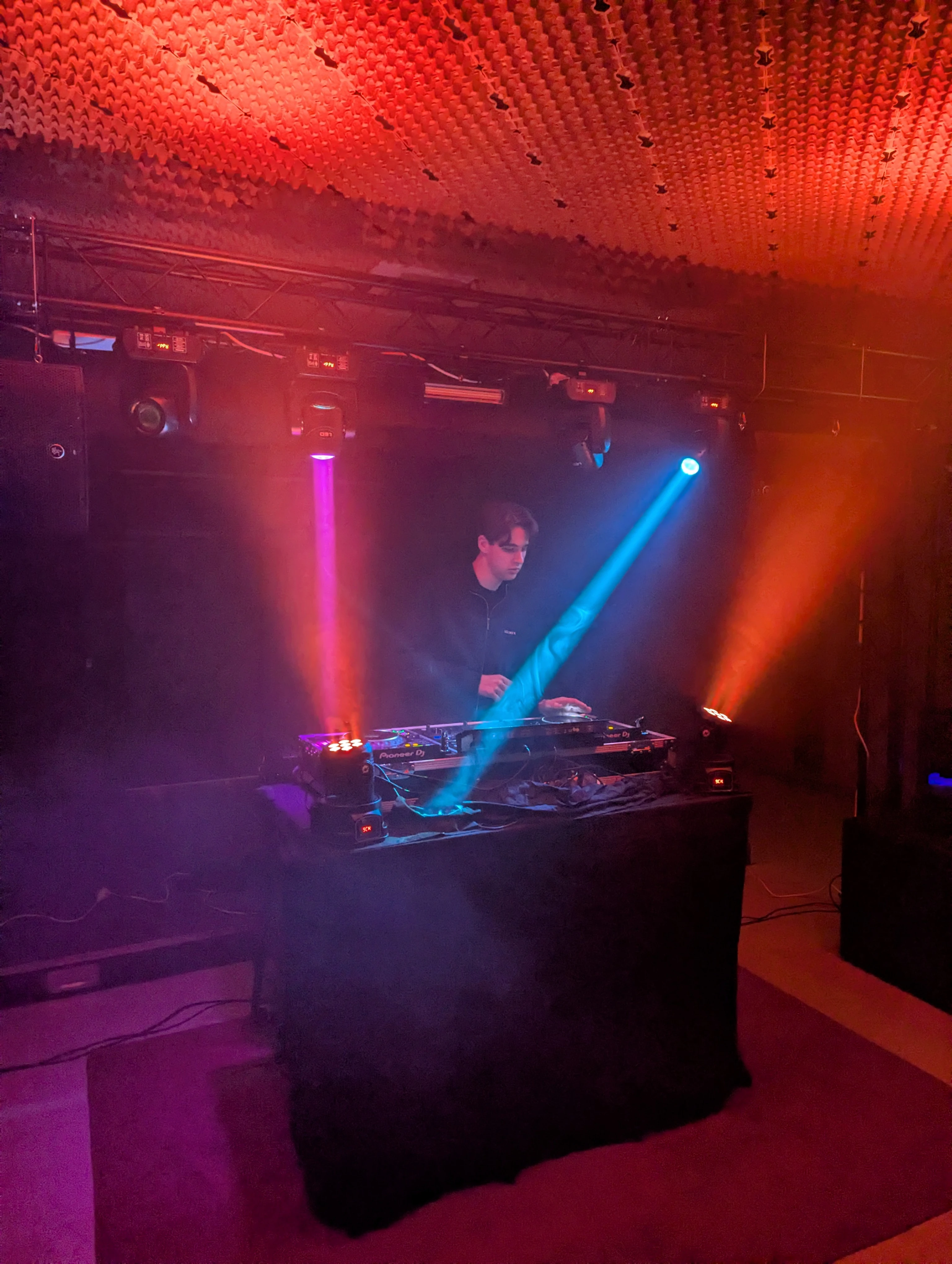DJ achter draaitafels op podium met rode en blauwe lichtstralen op kerstborrel