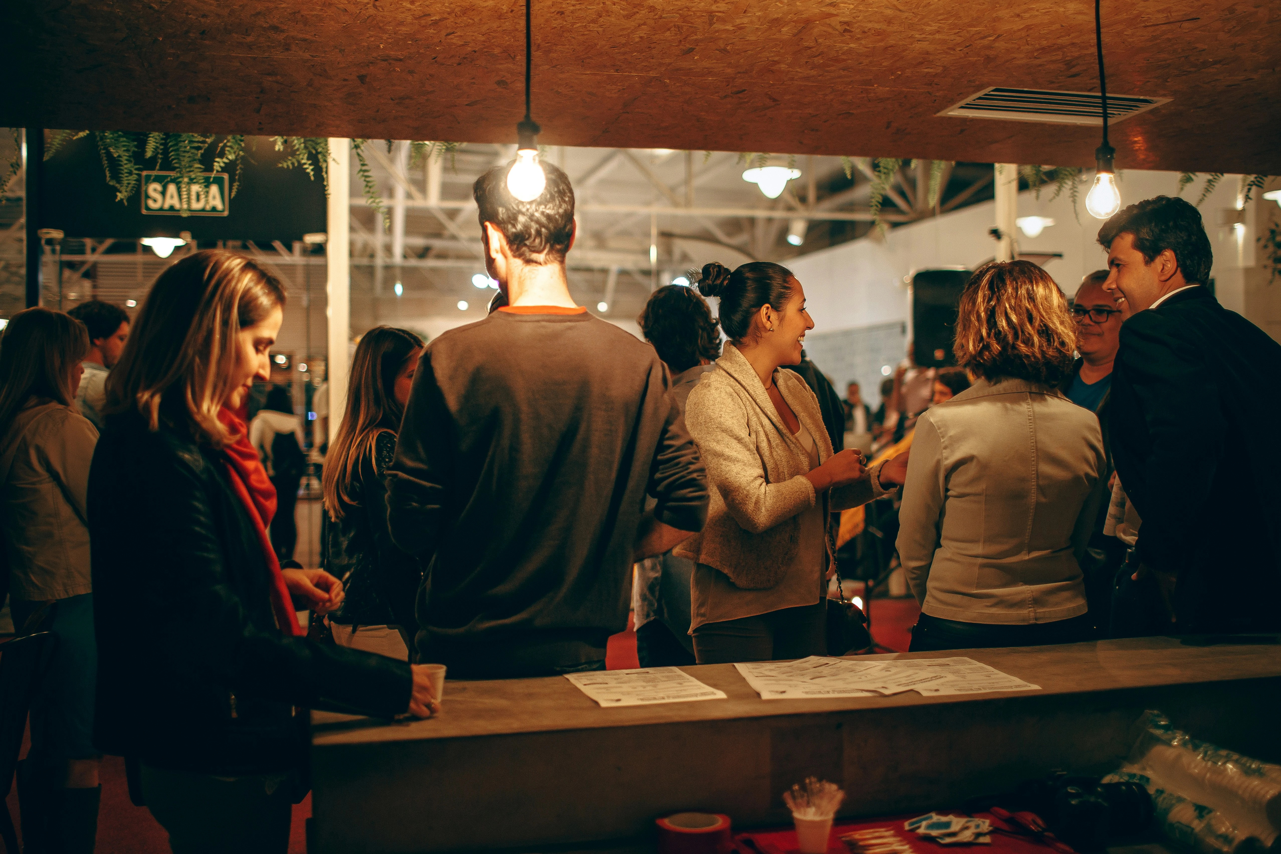 Gasten netwerken op informele borrel voor opening bedrijfspand onder warme hanglampverlichting