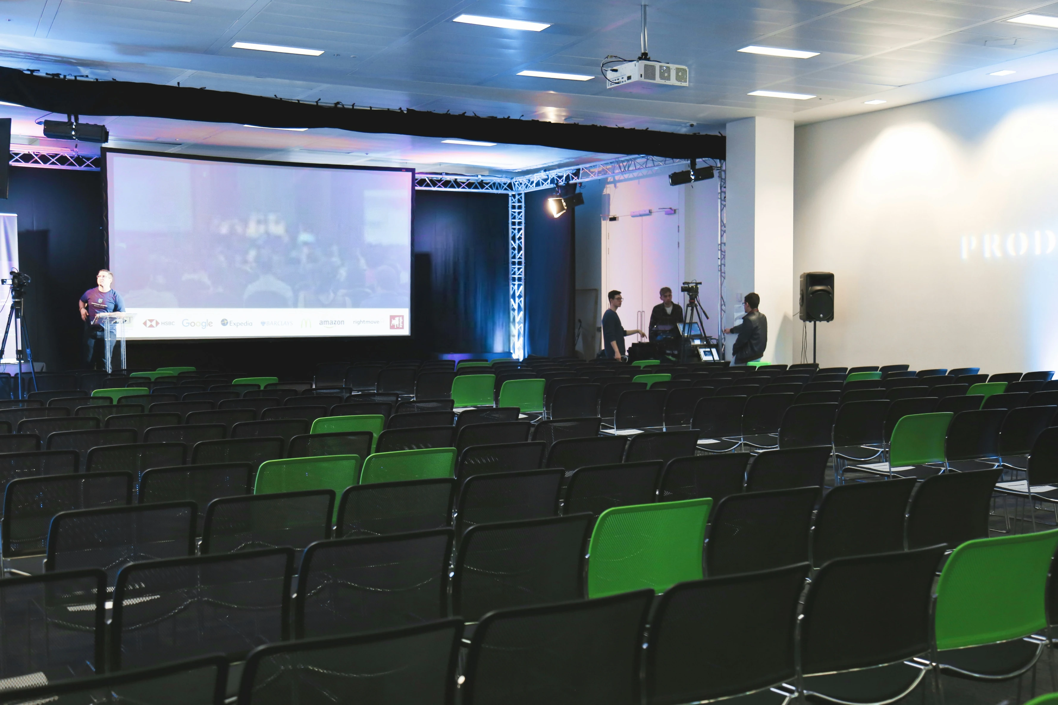 Presentator op podium op productlancering voor publiek met groen licht en groot scherm