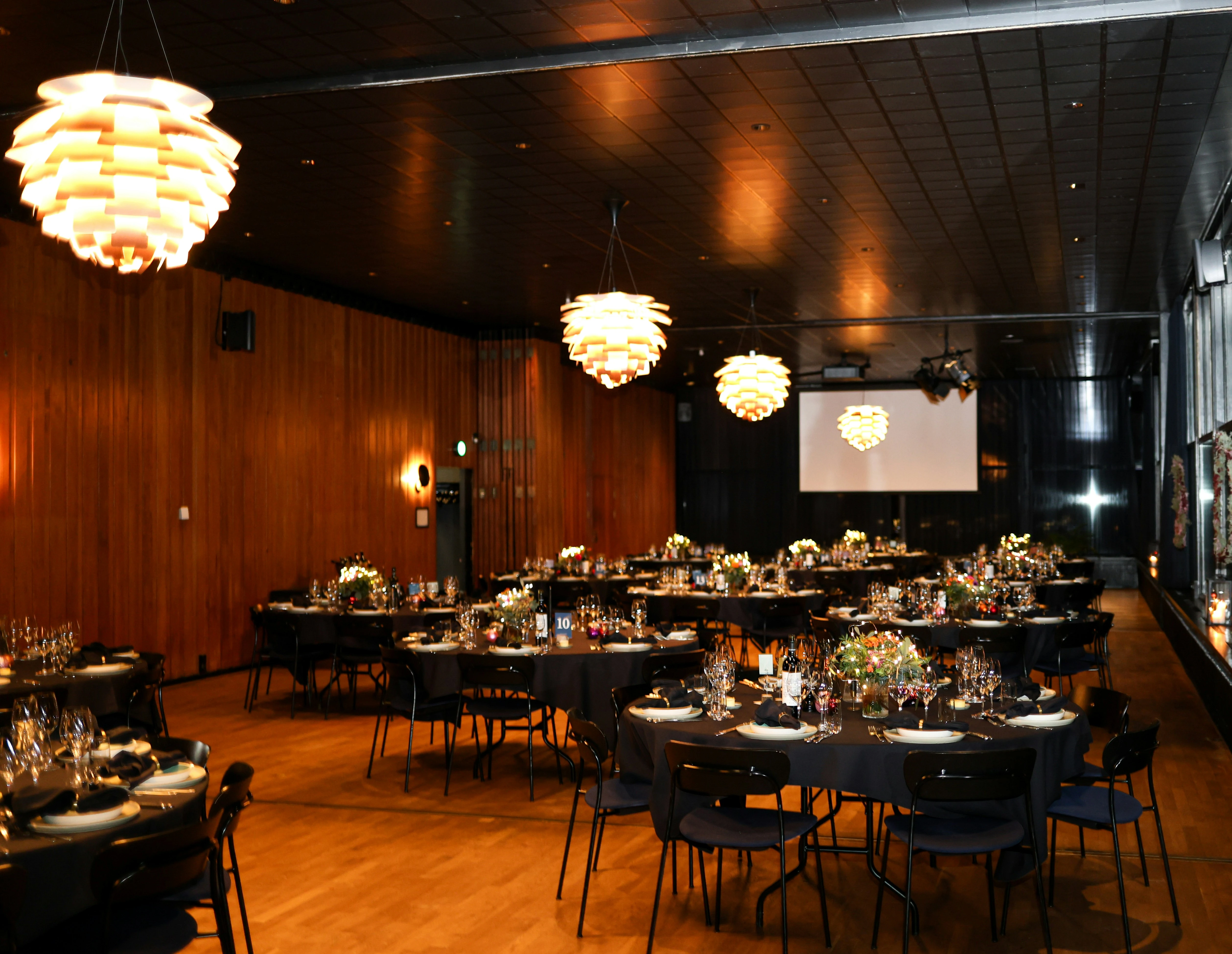 Gasten dineren aan tafels op productlancering in zaal met warme verlichting en hangllampen