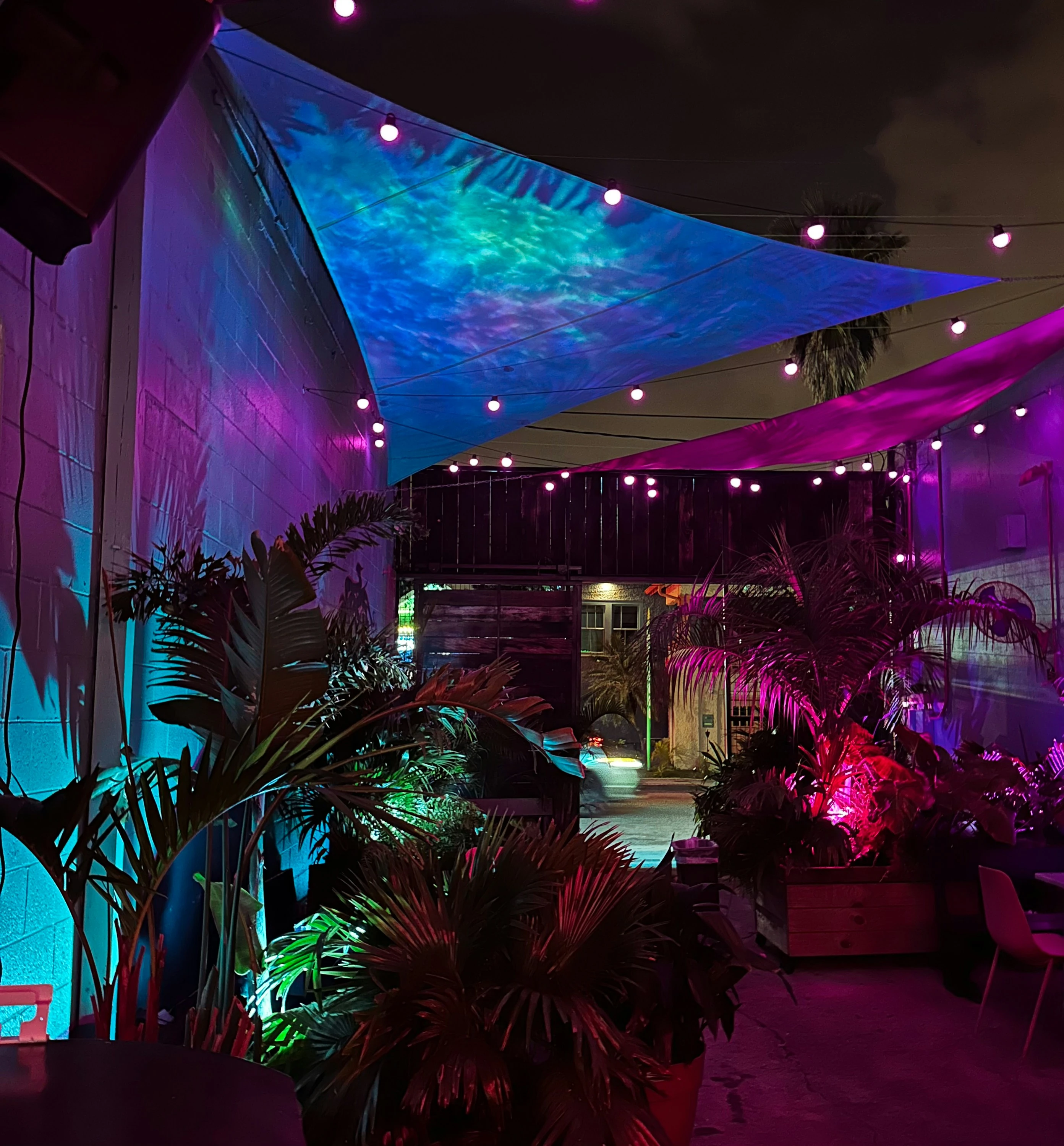 Tuinfeest op terras met kleurige zeilschermen, plantenbak en neonverlichting in blauw en roze