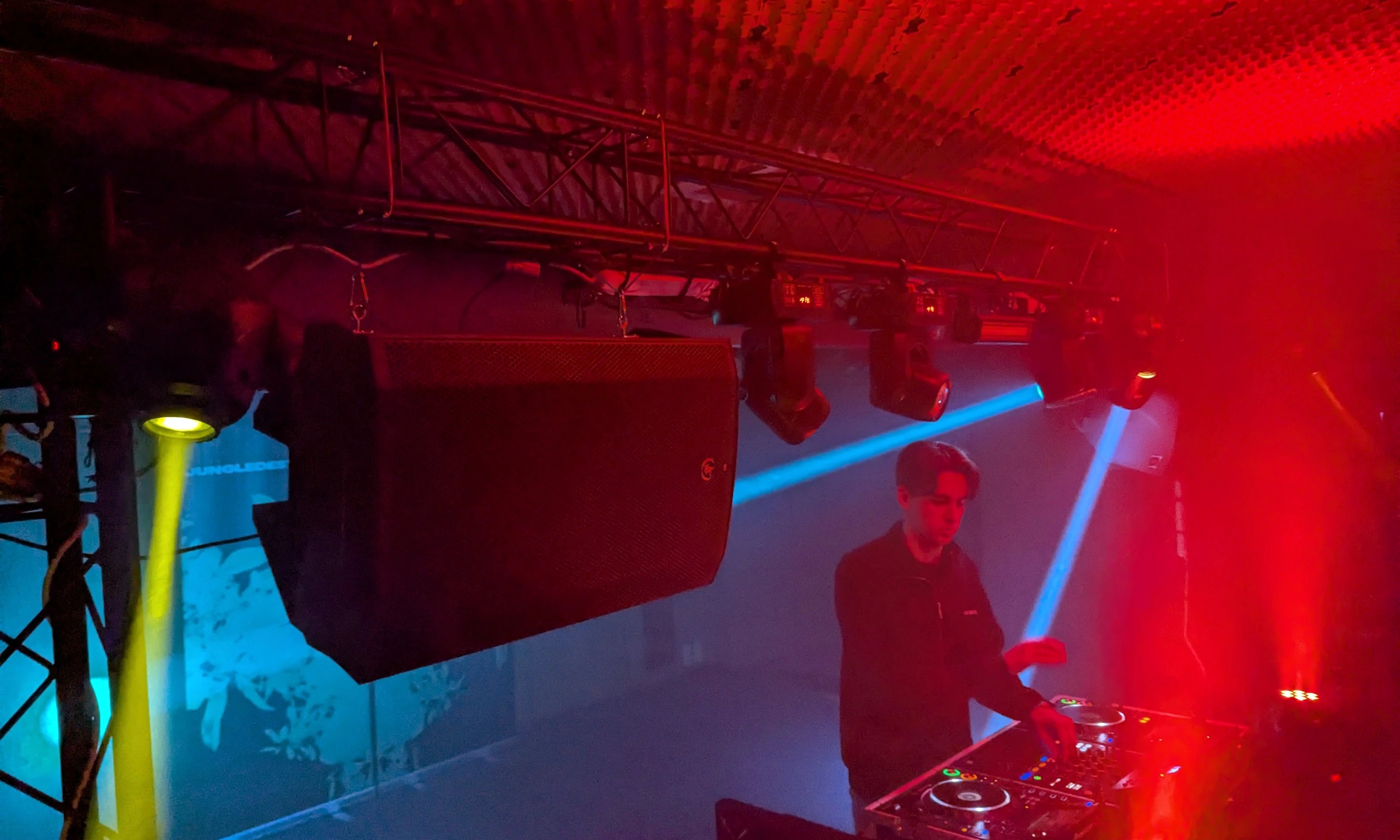DJ draait achter decks op tuinfeest onder rode en blauwe lichtstralen en trussconstructie