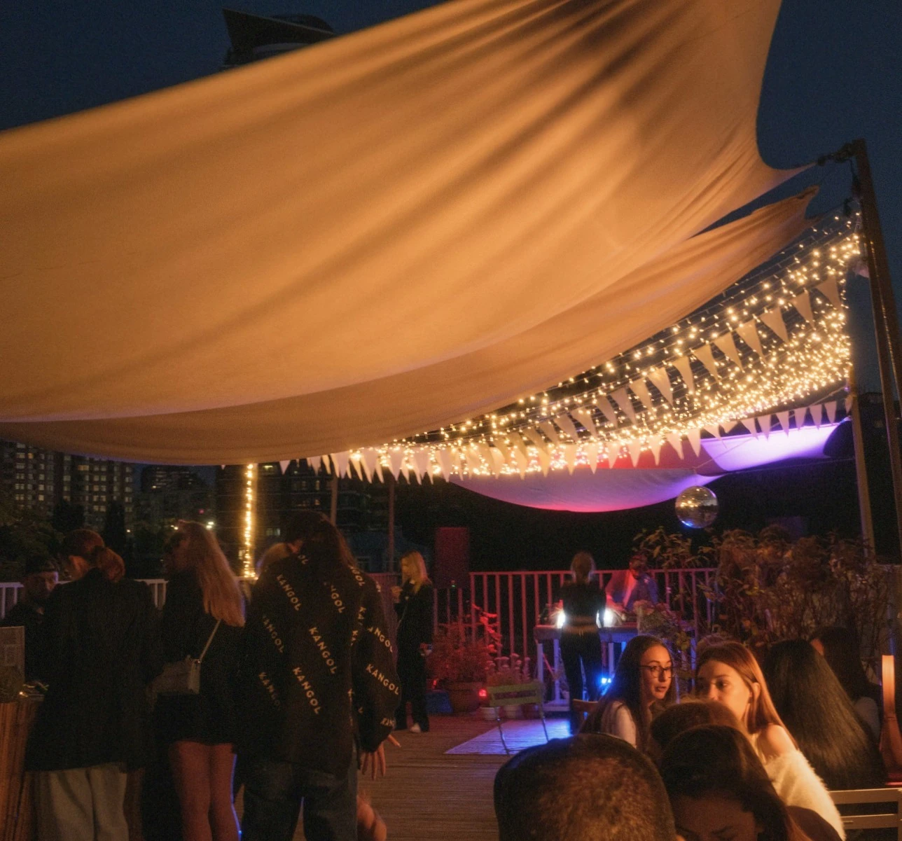 Gasten vieren tuinfeest onder verlichte tent met warme lichtslinger en gekleurde sfeerverlichting
