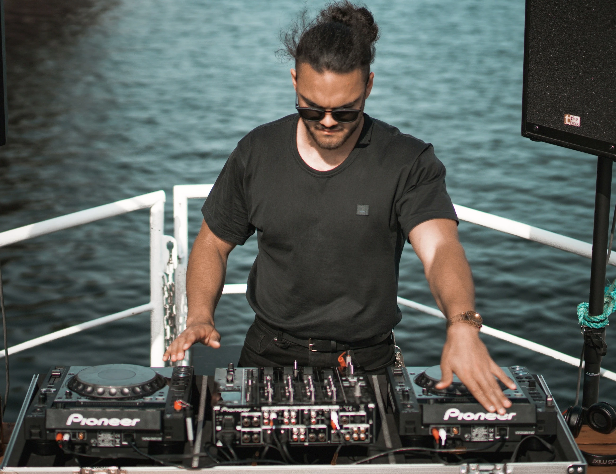 DJ with sunglasses and bun behind turntables on boat at yacht party
